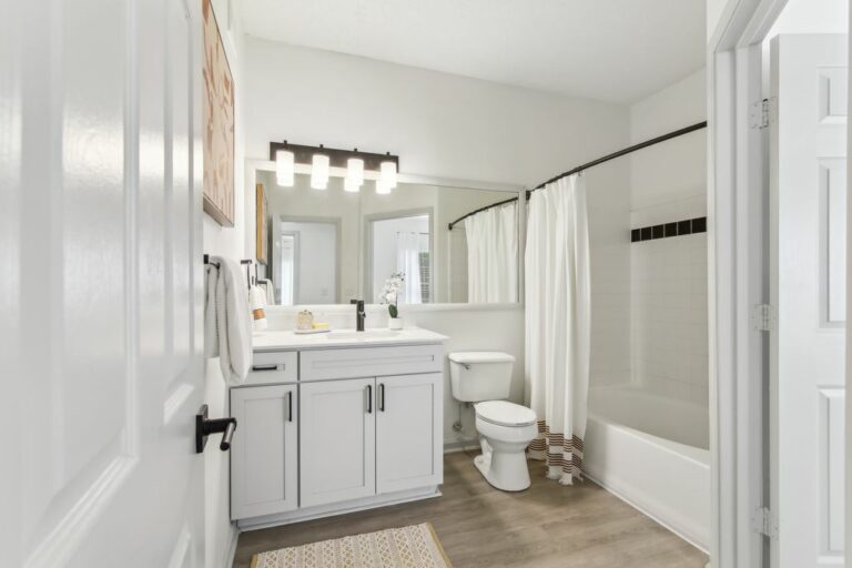 Virtually staged updated bathroom with toilet, tub, vanity mirror with vanity lighting, with white shaker cabinets with black accents.