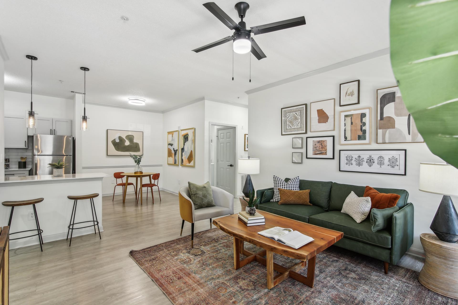 Renovated living room with furniture and wood-style flooring, with didnig room and open kitchen in the background.