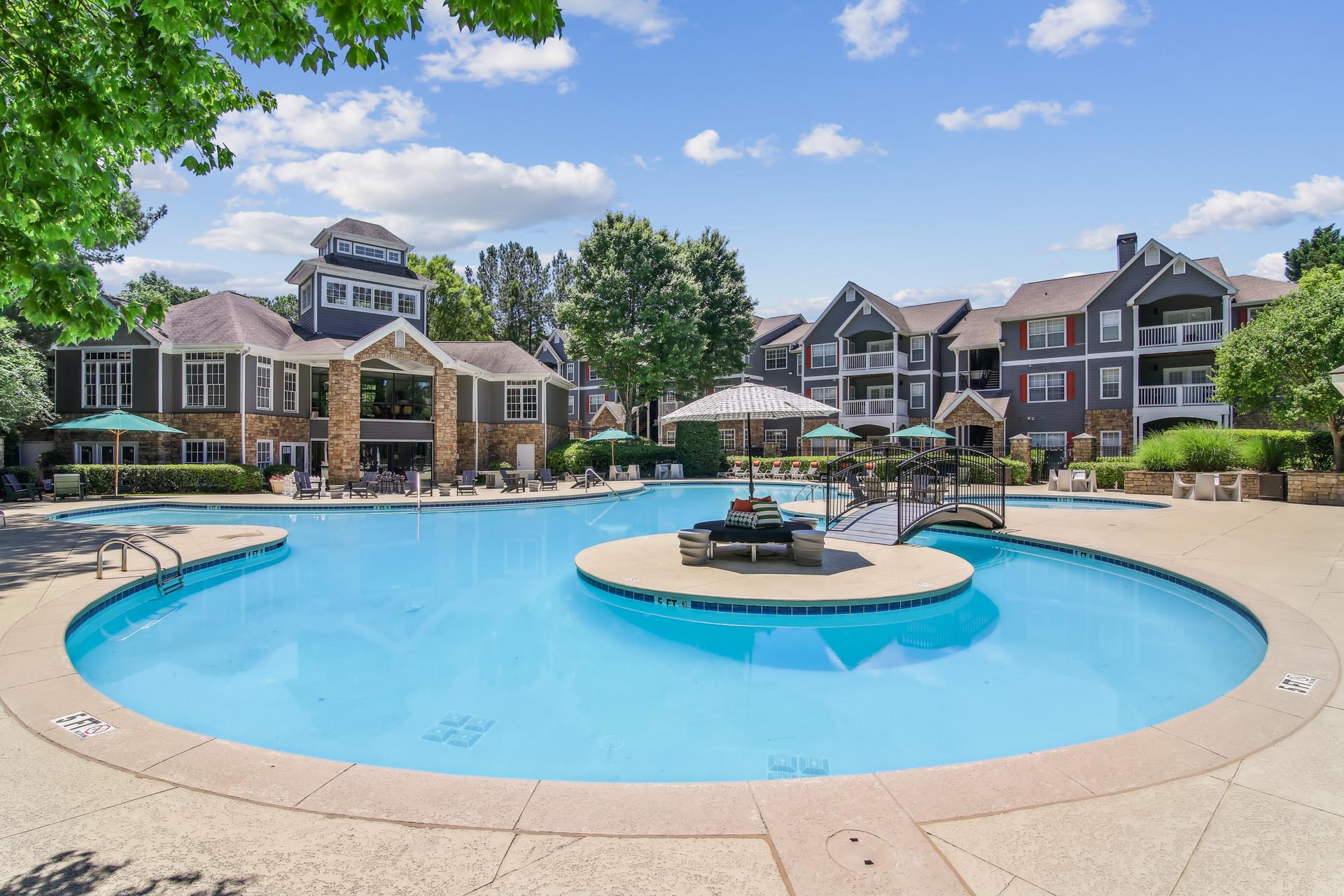 Swimming pool with sundeck and seating with leasing office and apartment buildings in background surrounded by native landscaping.