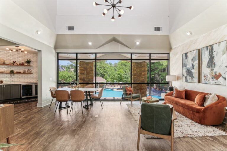 Clubroom with large table and seating area overlooking the swimming pool with clubroom kitchen in background.